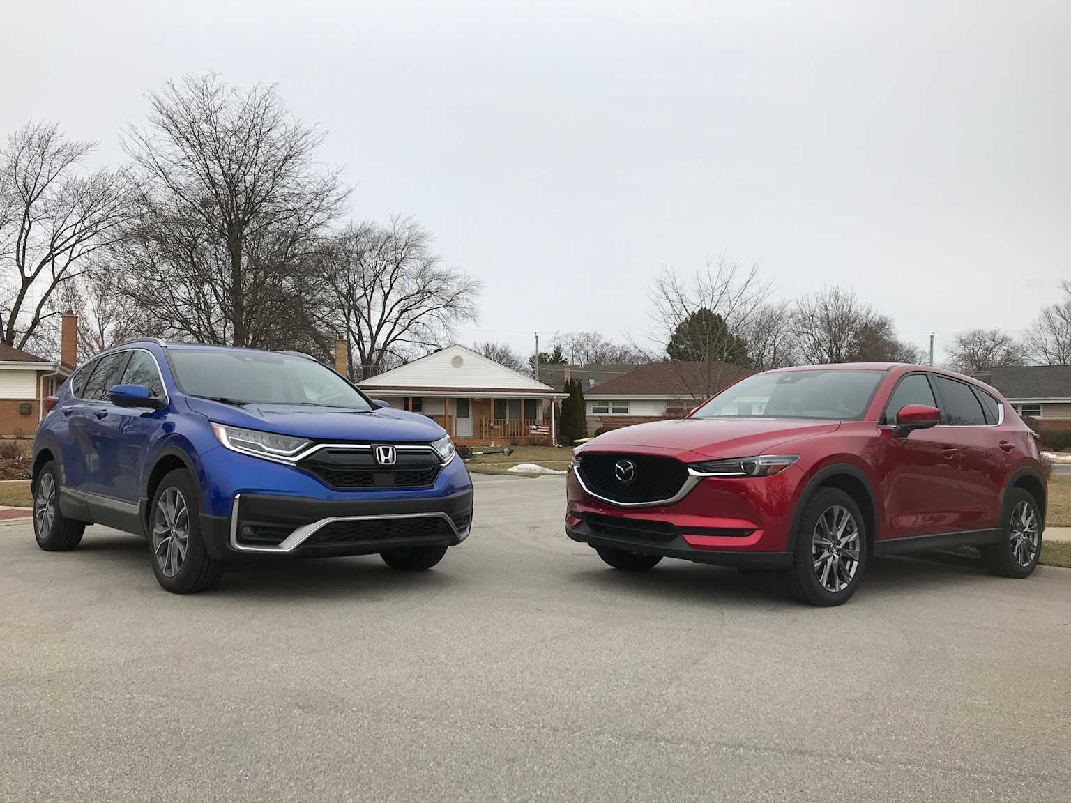 Giá xe Honda CR-V cũ cập nhật 3 Side-by-side comparison of a blue 2020 Honda CR-V and a red 2020 Mazda CX-5 in a suburban setting.
